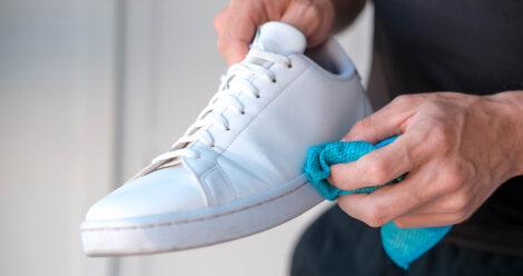 Weißer Sneaker wird mit einem blauen Tuch gereinigt.