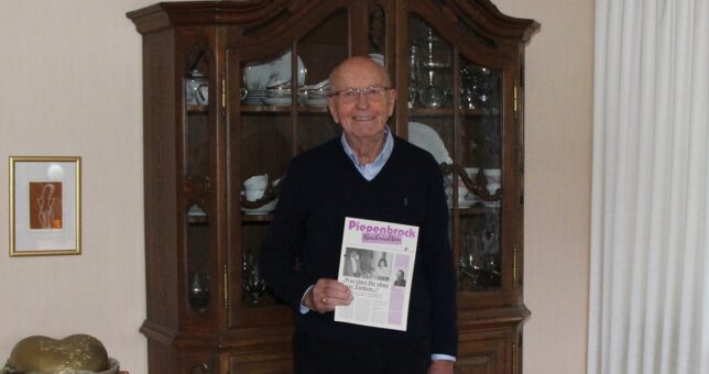 Ehemaliger Piepenbrock Niederlassungsleiter Georg Werning mit alter Ausgabe der Piepenbrock Nachrichten im Wohnzimmer vor einem Schrank.