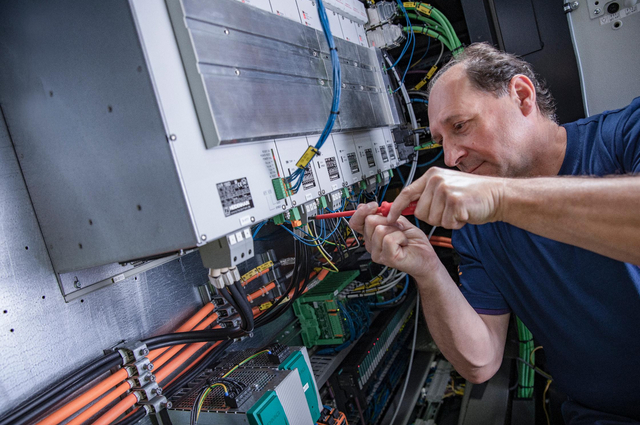 Mann schraubt mit einem Schraubenzieher an den Sicherungen einer elektrischen Maschine