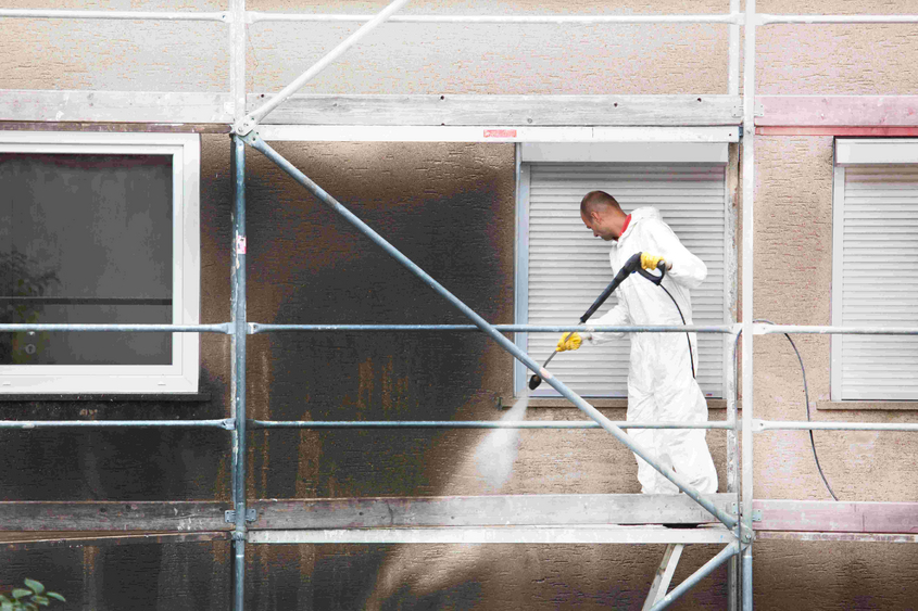 Piepenbrock Mitarbeiter reinigt verschmutzte Fassade auf Gerüst mit Hochdruckreiniger und entfernt Rußablagerungen