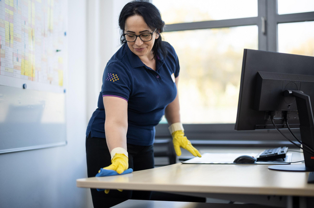 Frau wischt Büroarbeitsplatz ab