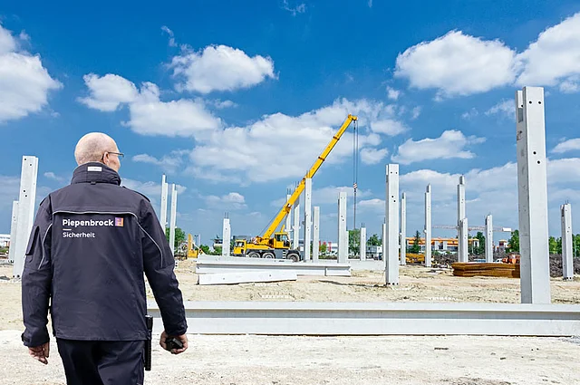 Person in Berufskleidung des Piepenbrock Sicherheitsdienst begeht Großbaustelle, auf der Kran steht