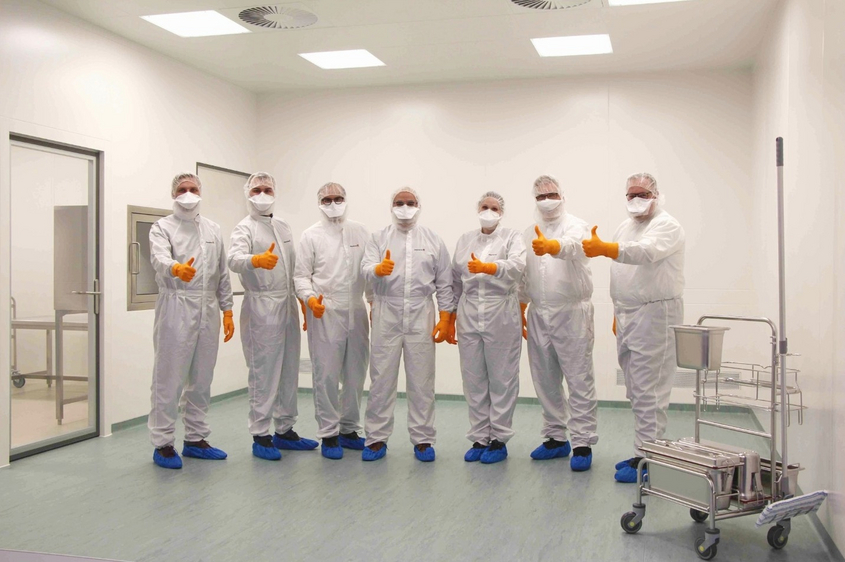 Team in Reinraumkleidung steht im Reinraum und zeigt Daumen hoch, hygienische Arbeitsumgebung