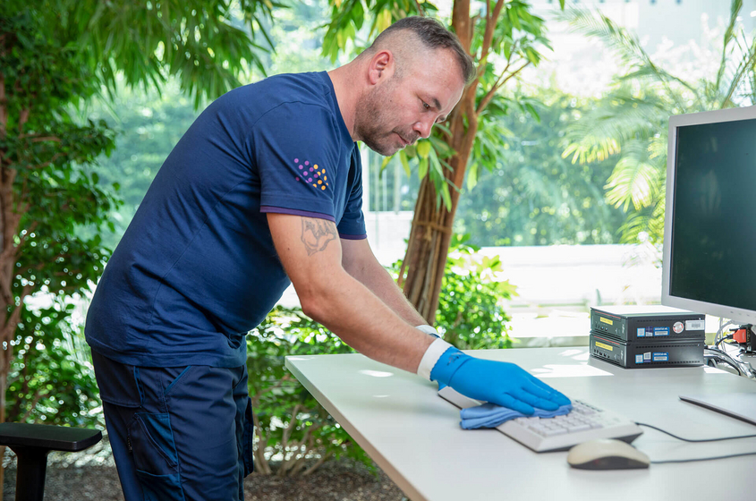 Mitarbeiter der Büroreinigung reinigt Tastatur und Arbeitsplatz