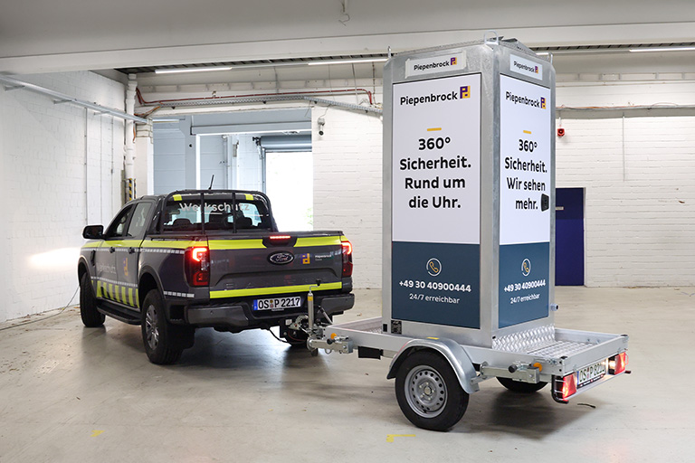Mobiler Videoturm auf Anhänger hinter einem Piepenbrock Werkschutzfahrzeug in einer Halle